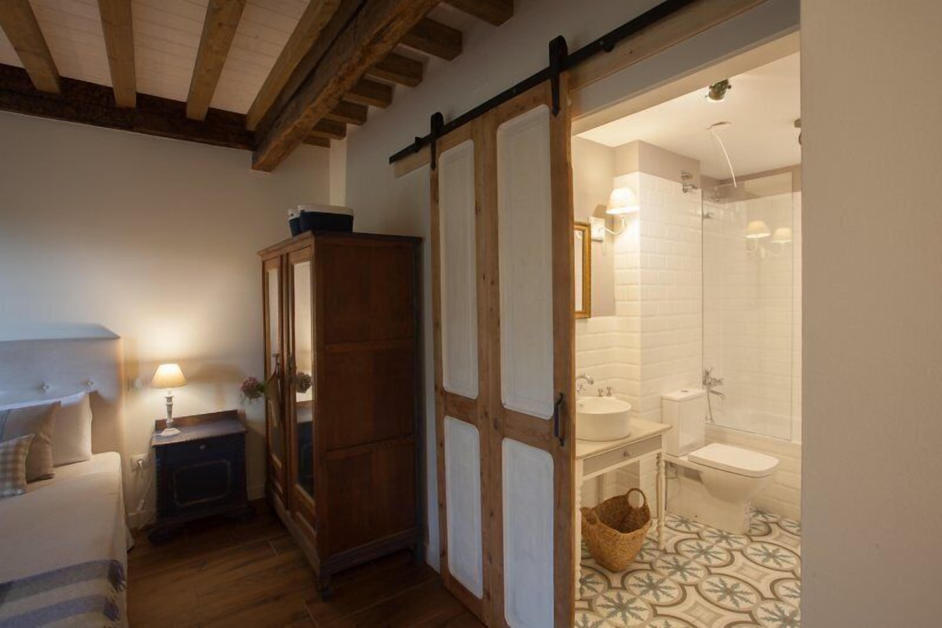 A bedroom with a bed, a wooden wardrobe, and a nightstand with a lamp.