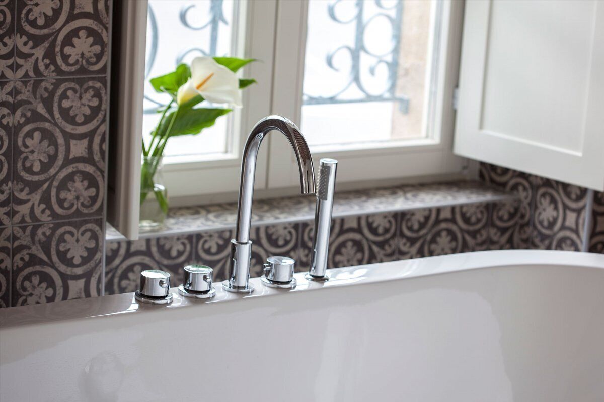A bathroom with a white bathtub, a window with a view of a balcony, and patterned tiles.