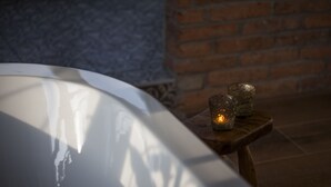 A white bathtub with a wooden stool beside it, a brick wall, and a tiled floor. - Posada Seis Leguas (Cartes)