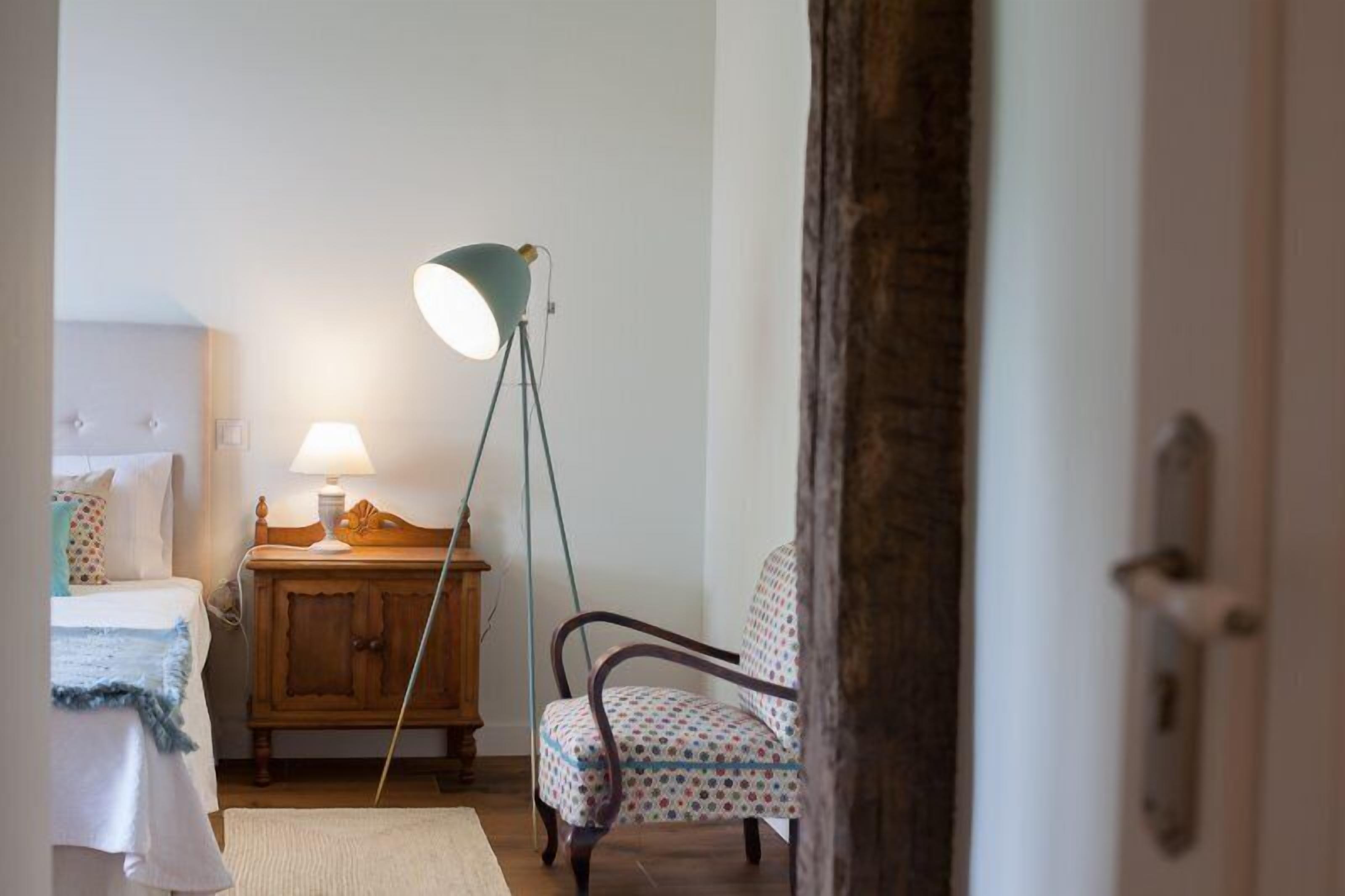 A bedroom with a bed, bedside table, lamp, chair, and a wooden cabinet.