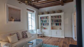 A cozy living room with a white sofa, a glass coffee table, and a bookshelf filled with books.