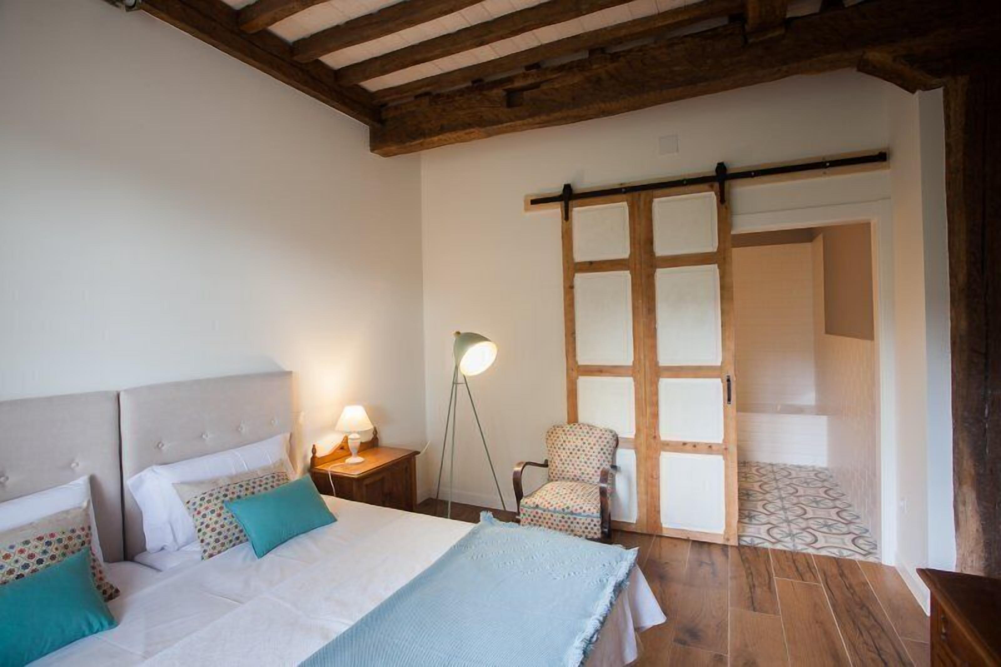 A bedroom with a bed, bedside tables, a chair, a lamp, and a sliding door leading to another room.