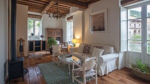 A cozy living room with a wooden ceiling, a fireplace, a white sofa, and a view of a building through large windows. - Posada Seis Leguas (Cartes)