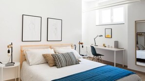 Un dormitorio moderno con cama, mesitas de noche, escritorio y una silla. Hay dos cuadros en la pared.