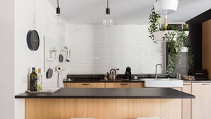 A modern kitchen with a black countertop, wooden cabinets, and a white backsplash. There are two stools, a kettle, and a coffee maker on the counter. - The Bike garage ✦ Sum (Milano)