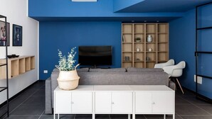 A modern living room with a blue accent wall, a flat-screen TV, a grey sofa, white cabinets, and a plant. - The Bike garage ✦ Sum (Milano)