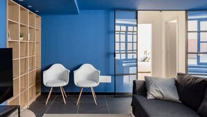 A modern living room with a blue accent wall, a sofa, two white chairs, a TV, and a bookshelf. - The Bike garage ✦ Sum (Milano)