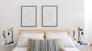 A bedroom with a wooden headboard, two bedside tables with lamps, a bed with patterned bedding, and two framed artworks on the wall. - The Bike garage ✦ Sum (Milano)