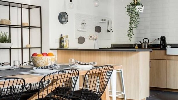 A modern kitchen with a central island, black wire chairs, and a hanging plant. - The Bike garage ✦ Sum (Milano)
