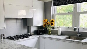 Una cocina moderna con armarios blancos, encimera de mármol, estufa a gas y ventana con vistas a zonas verdes.