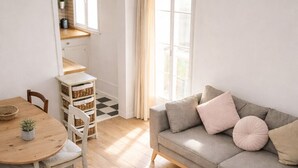 Ein Wohnzimmer mit einem runden Holztisch, einem grauen Sofa mit Kissen und einem kleinen runden Couchtisch auf Holzdielen.