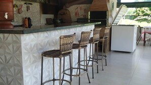 A kitchen area with a bar counter, three wicker stools, a large water dispenser, and a built-in oven. - SÍTIO DO IPÊ, please contact us before booking!!! (Residencial são vicente)