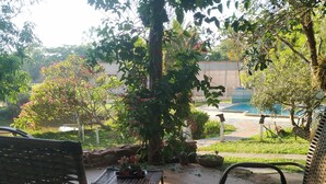 A patio area with two wicker chairs and a small table, surrounded by lush greenery and a view of a pool. - SÍTIO DO IPÊ, please contact us before booking!!! (Residencial são vicente)