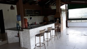 A kitchen with a bar area, white patterned tiles, and wicker bar stools. - SÍTIO DO IPÊ, please contact us before booking!!! (Residencial são vicente)