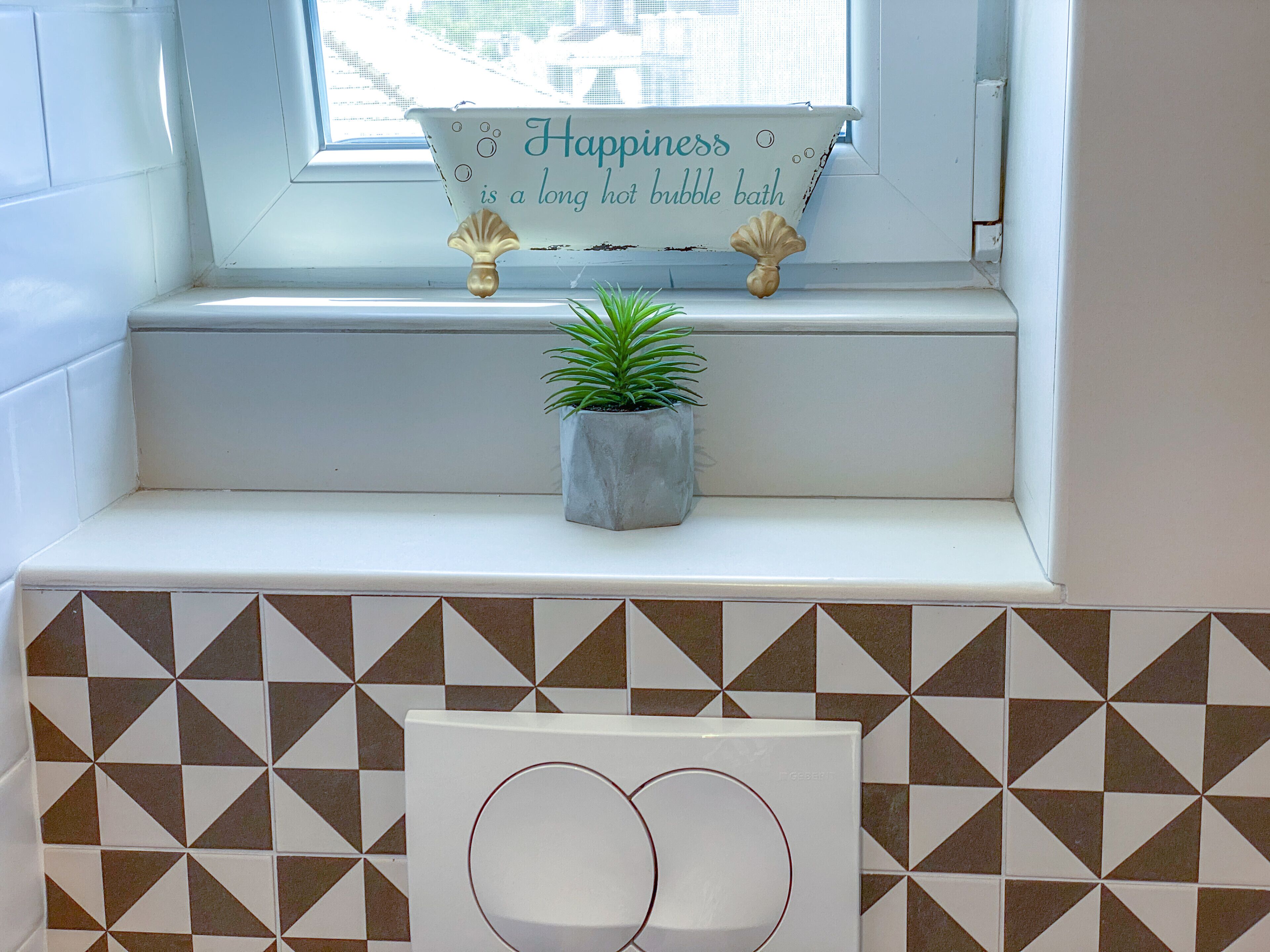 Un baño con un alféizar, una planta en maceta y un cartel que dice “La felicidad es un baño de burbujas largo y caliente.”