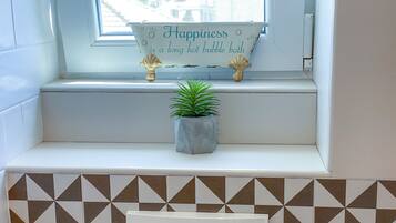 Un baño con un alféizar, una planta en maceta y un cartel que dice “La felicidad es un baño de burbujas largo y caliente.”