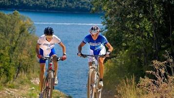 Dos ciclistas en un sendero de montaña con un lago y un bosque al fondo.