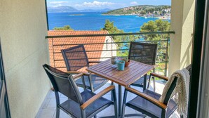 Een balkon met een tafel en stoelen, met uitzicht op een kustplaatsje en de zee.