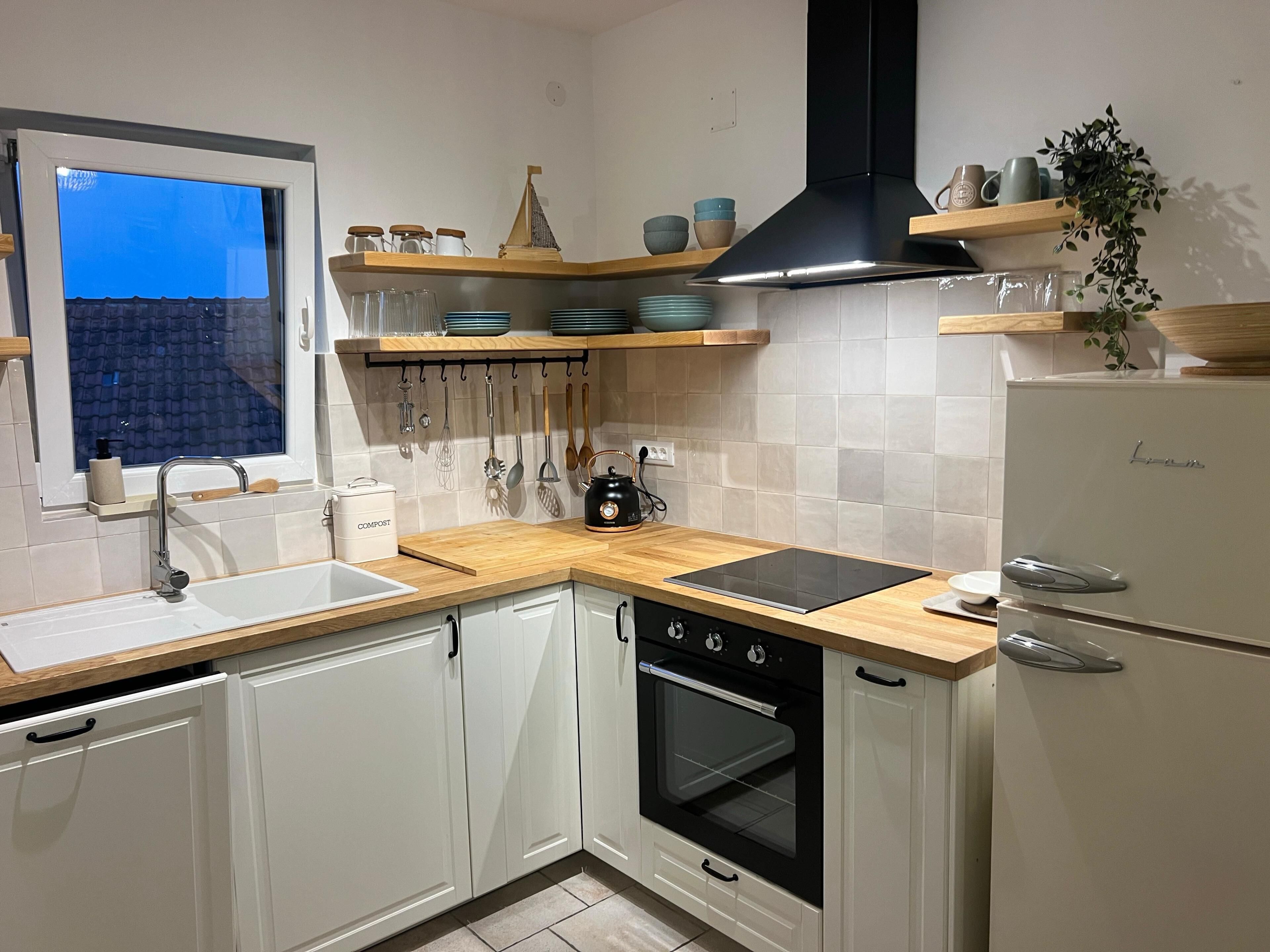 Een keuken met witte kasten, een zwarte kookplaat, een spoelbak en een raam met uitzicht op een blauwe lucht.