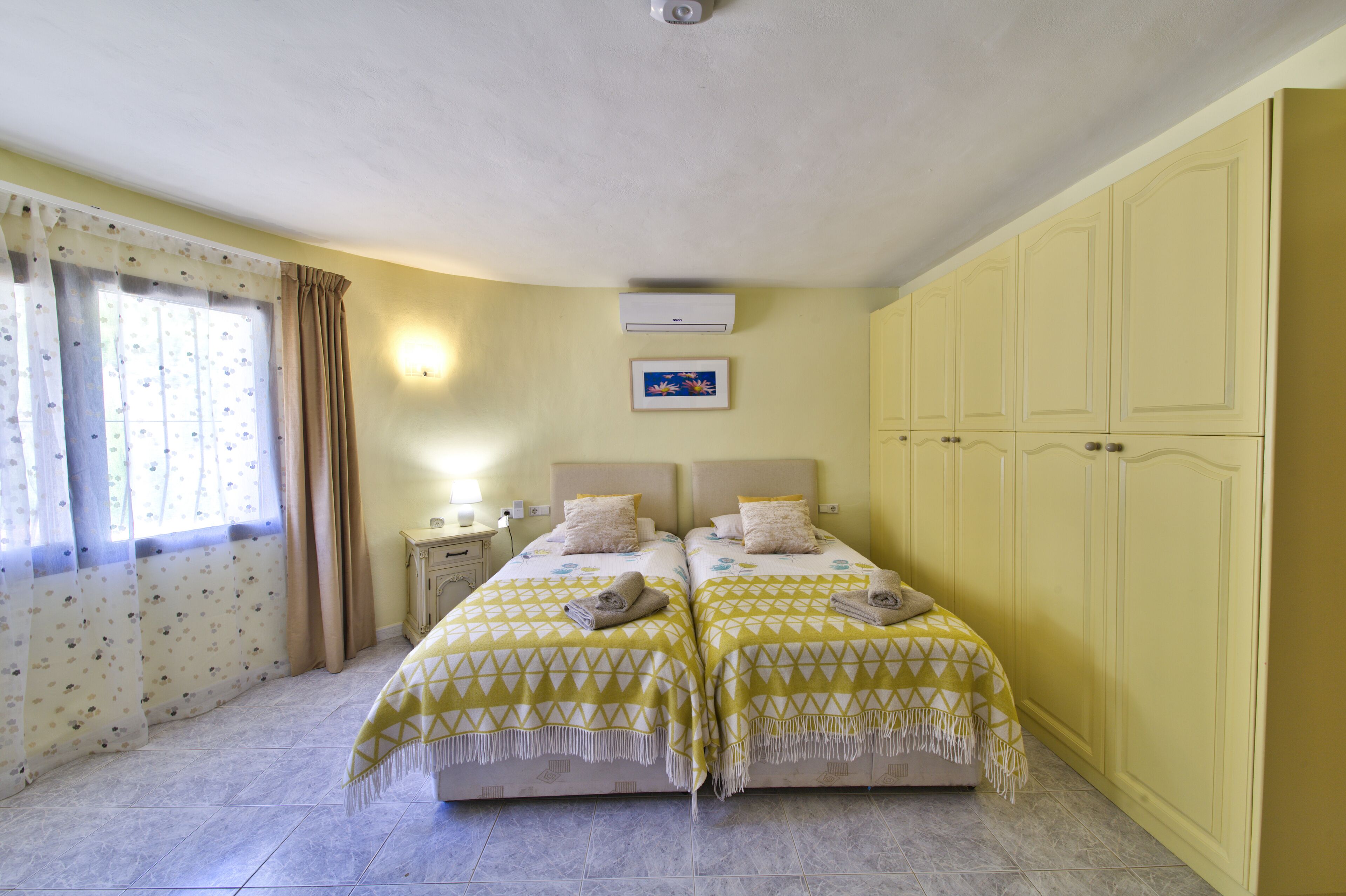 Une chambre avec deux lits, une table de chevet, un climatiseur fixé au mur et une fenêtre avec des rideaux.