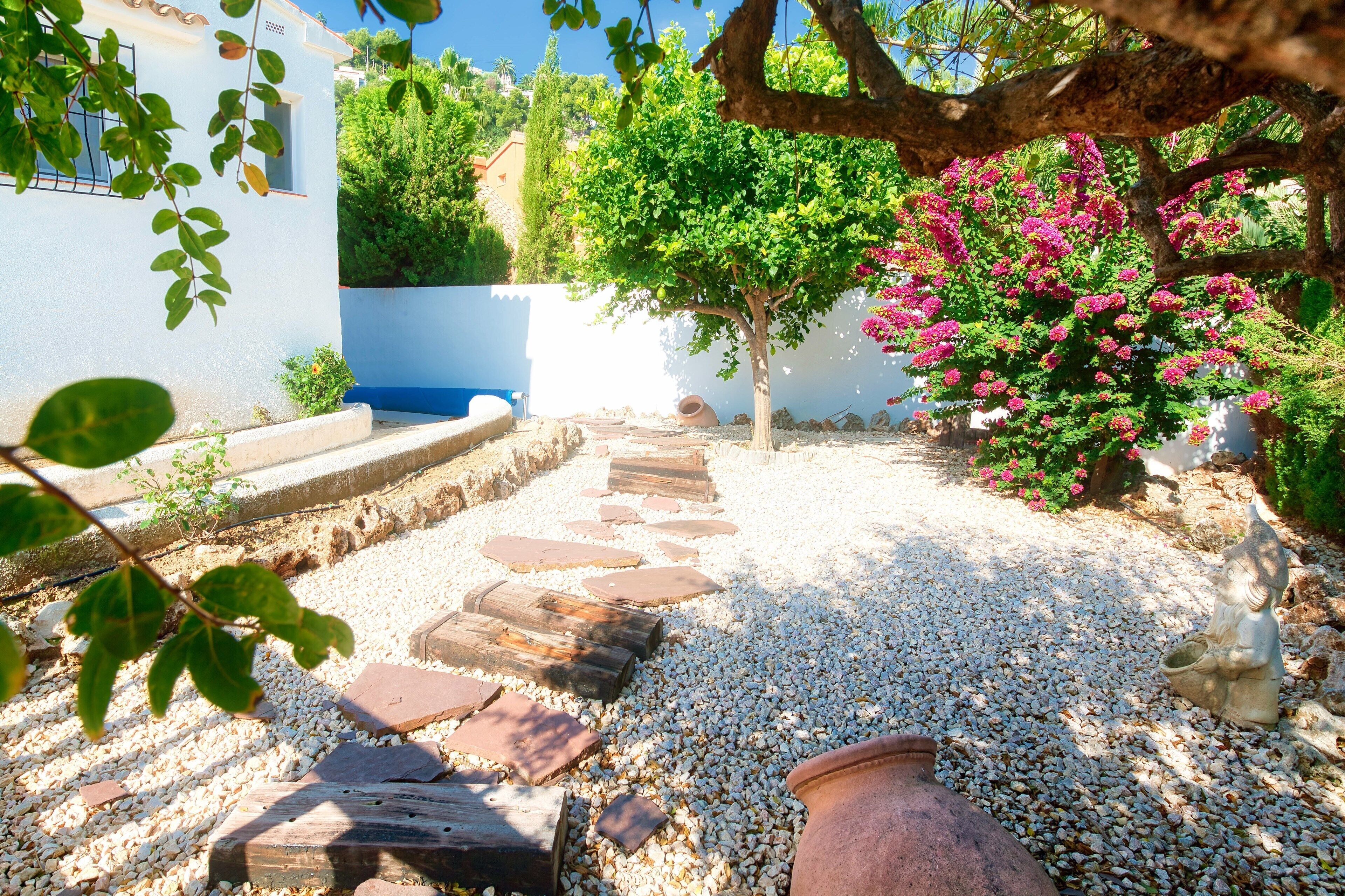 Un sendero en el jardín con piedras para pisar, un árbol y una estatua.