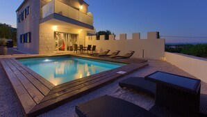 A modern building with a swimming pool, lounge chairs, and a table. - Pax house with private pool 2 (Krk)