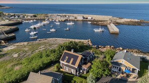 An aerial view of a coastal town with a marina, houses, and a rocky shoreline.