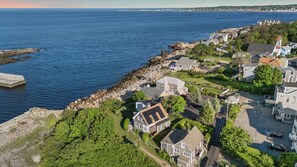 A coastal residential area with houses, a rocky shoreline, and a view of the sea.