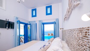 A hotel room with a bed, a TV, a view of the sea, and a balcony with chairs.