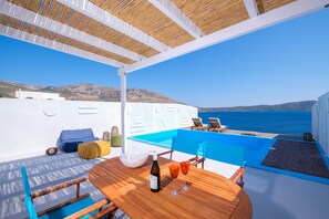 A sunlit outdoor seating area with a wooden table, chairs, and a view of the sea. - Aelia Collection Suites - Adults Only (Skiros)