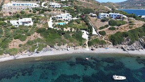 An aerial view of a coastal area with modern white buildings, a clear blue sea, and a sandy beach.