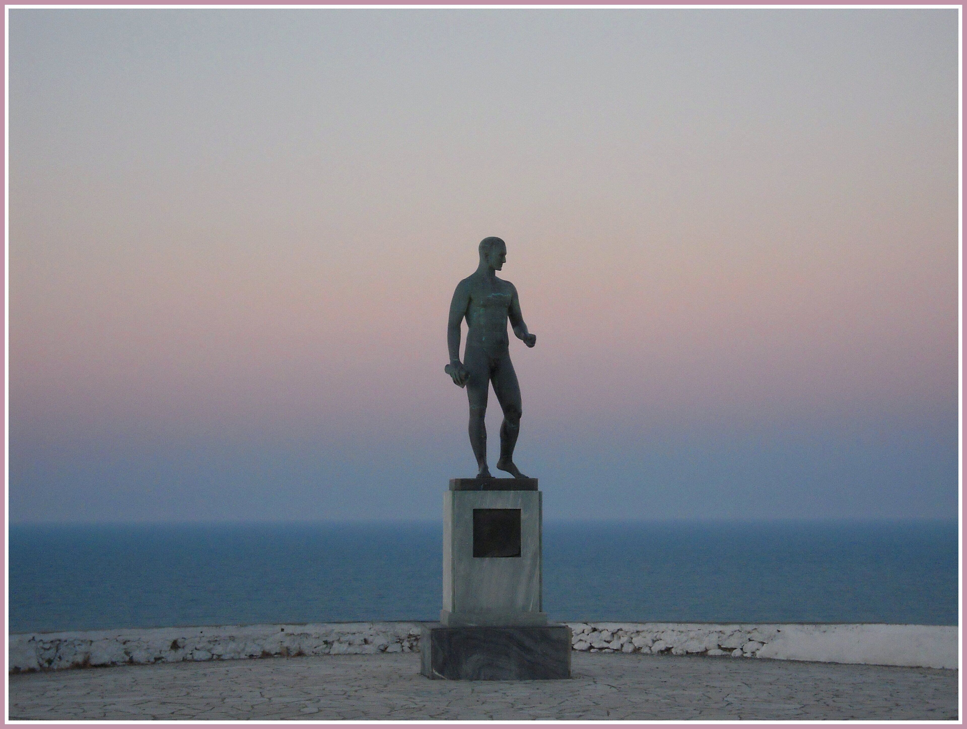 A statue on a pedestal by the sea.