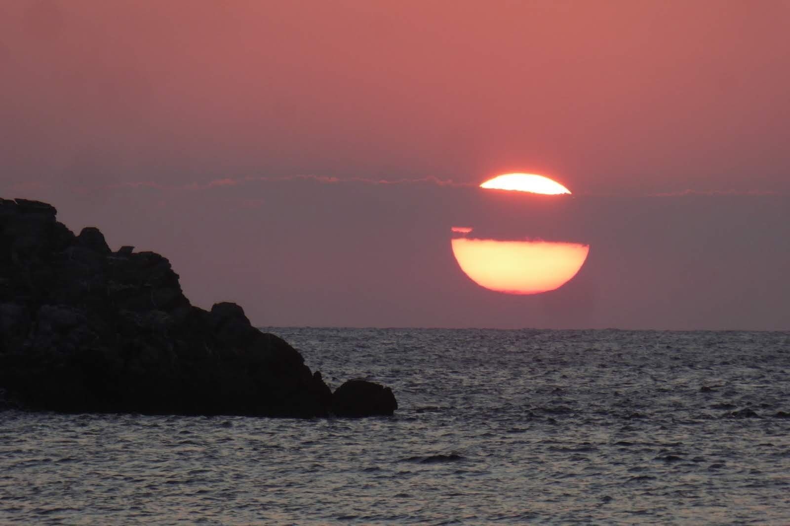 A sunset over the ocean with a rocky coastline.
