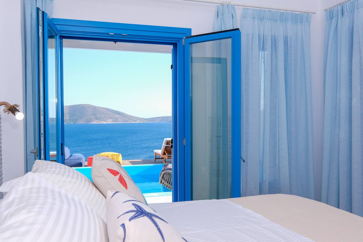 Une chambre avec un grand lit, une vue sur la mer et un balcon avec une piscine.
