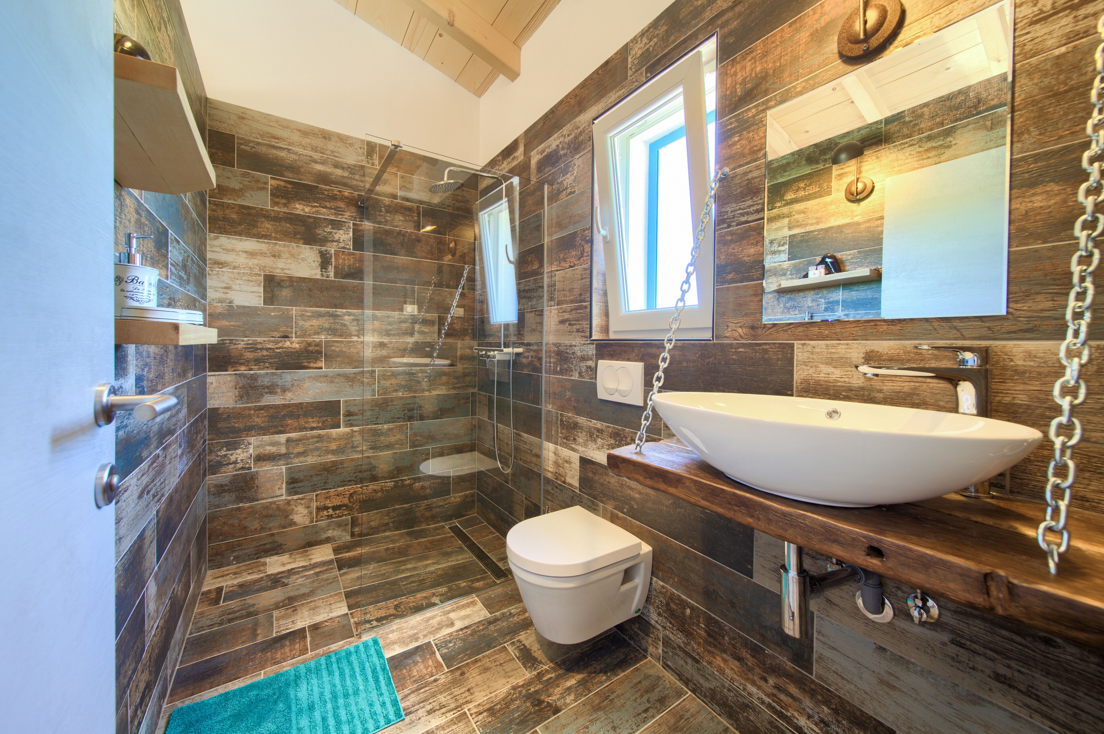 A modern bathroom with a wooden floor, a white sink, and a glass shower enclosure.