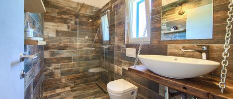A modern bathroom with a wooden floor, a white sink, and a glass shower enclosure.