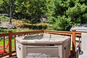 A spa hot tub with a wooden deck and railing, surrounded by greenery and rocks.