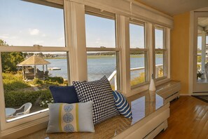 A room with a view of a lake, a bench with cushions, and a wooden floor. - Sunset Cove: Waterfront living on the Annisquam River (Gloucester)
