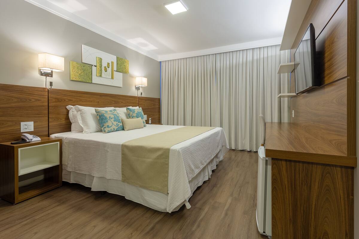 Une chambre d’hôtel avec un lit, des tables de chevet, un bureau, une télévision et des rideaux.