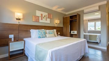 Quarto de hotel com uma cama grande, mesas de cabeceira, guarda-roupa, ar condicionado e uma janela com cortinas.