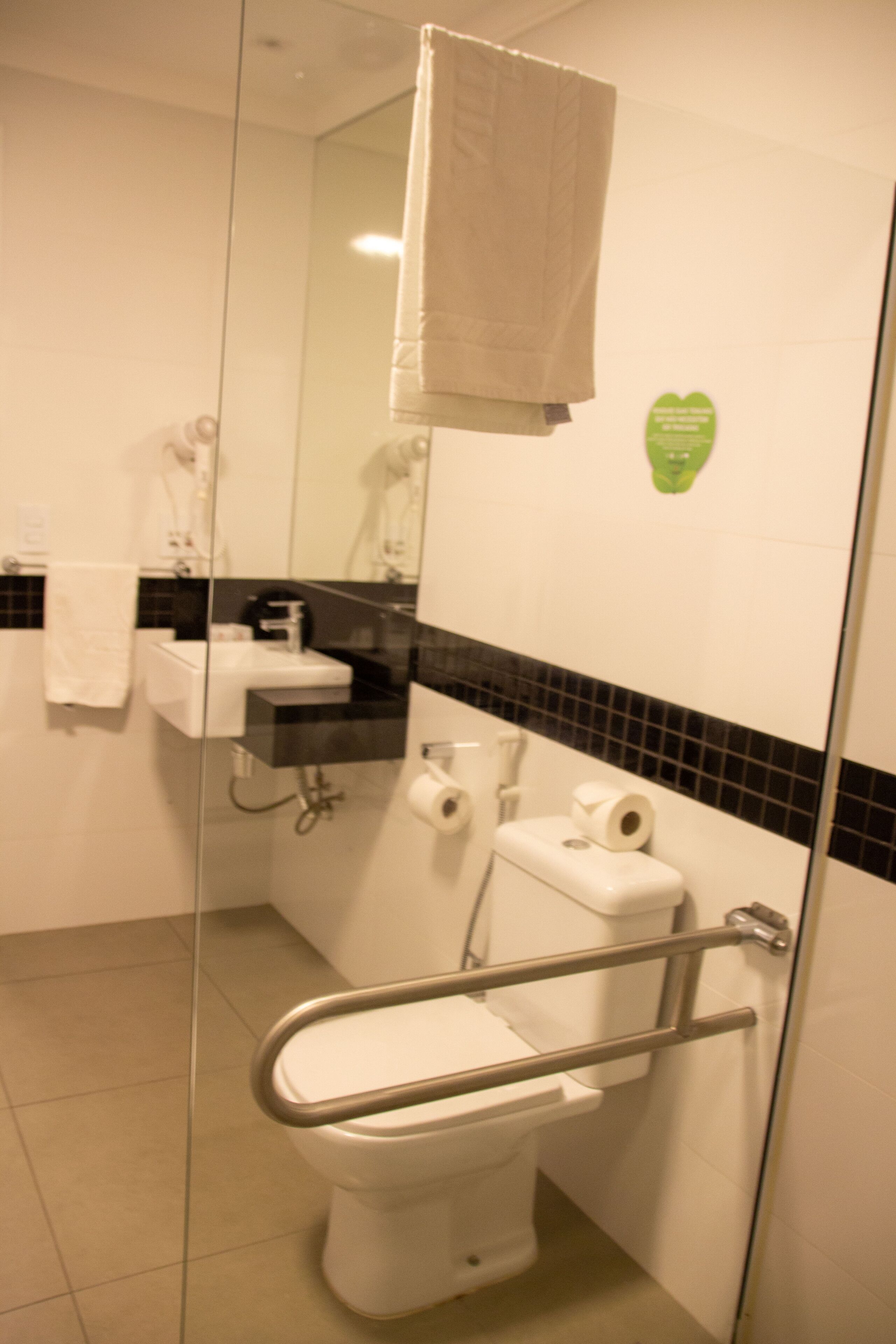 Een badkamer met een glazen scheiding, een wit toilet, een wastafel en een handdoek aan de muur.