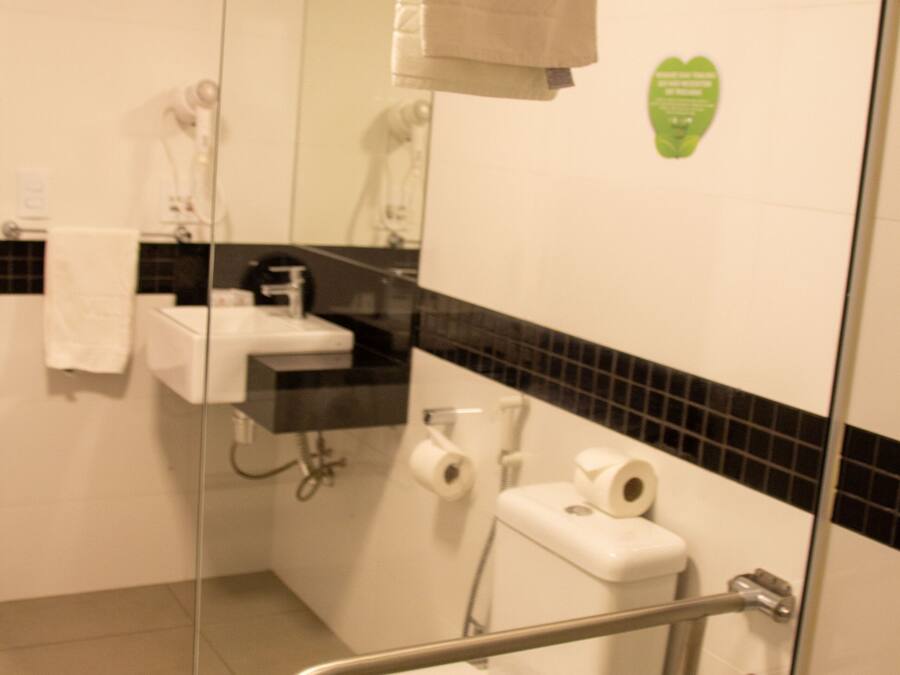 Un baño con mampara de vidrio, inodoro blanco, lavamanos y una toalla colgada en la pared.