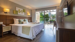 Een moderne hotelkamer met een groot bed, een bureau en een balkon met uitzicht op de stad.