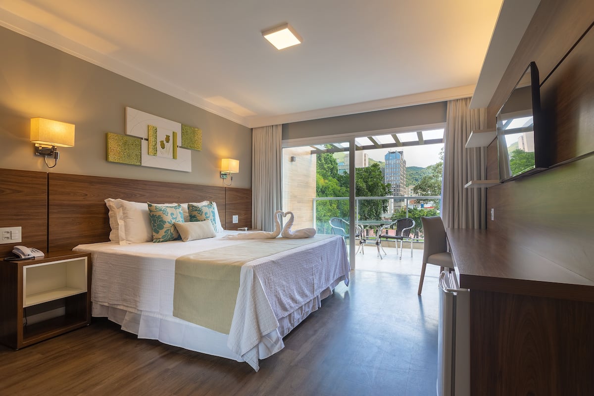 Une chambre d’hôtel moderne dotée d’un grand lit, d’un bureau et d’un balcon offrant une vue sur la ville.