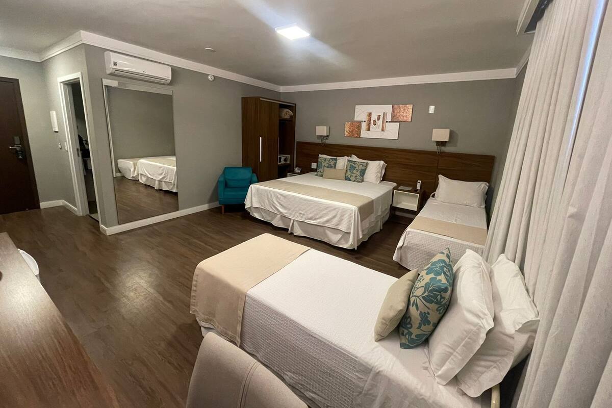 Une chambre d’hôtel avec deux lits simples, un coin salon avec un fauteuil, une armoire et un miroir.