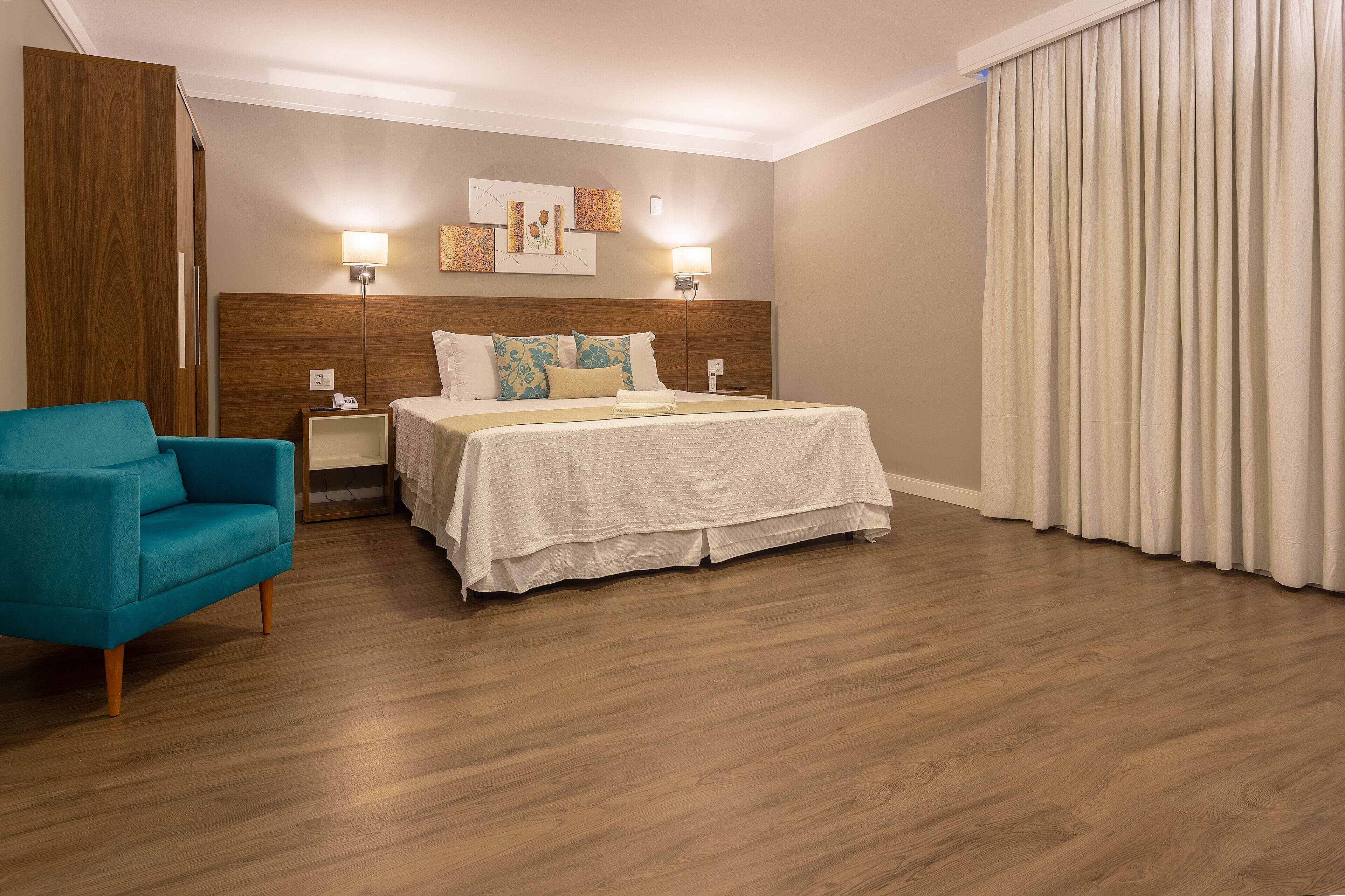 Una habitación de hotel con una cama, una mesita de noche, un sillón azul y un armario de madera.