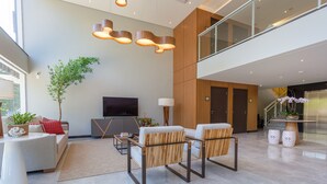 Een moderne hotellobby met een zithoek, een flatscreen televisie en een trap naar een hoger gelegen verdieping.
