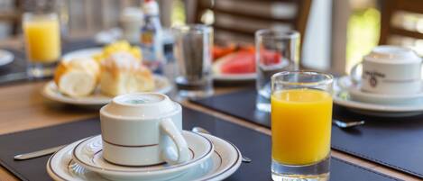 Un desayuno con una taza de té, croissants y jugo de naranja sobre una mesa.