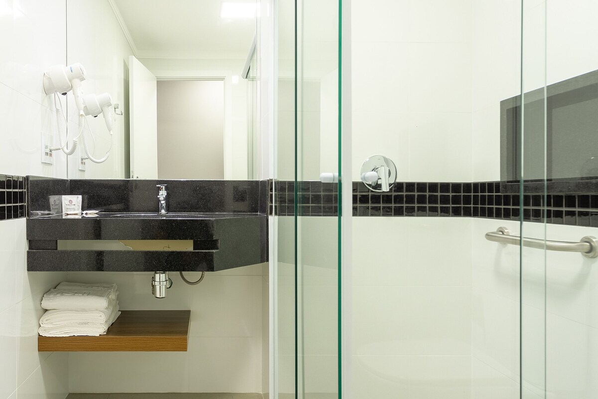Un baño moderno con ducha de vidrio, tocador con encimera negra y un perchero para toallas.