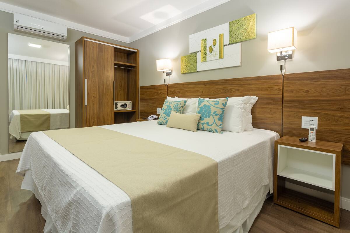 Une chambre d’hôtel avec un lit, des tables de chevet, une armoire et un miroir.